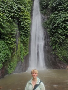 Tanah Barak Waterfall in Munduk, 75 feet tall, pouring down a cliff covered in green leafy vines. Emmons is in front, dwarfed by the waterfall.